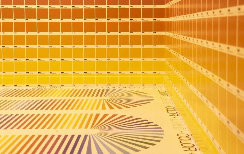 A room wallpapered with Pantone color swatches; monochromatic and engulfed in a yellow hue, essentially eliminating the existence of all other colors.