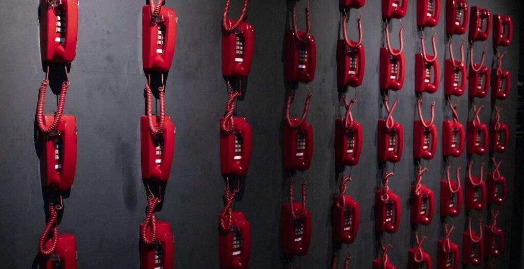 A wall with red corded landline phones mounted in a grid pattern.
